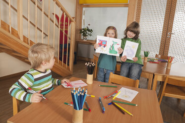 Deutschland, Kinder im Kinderzimmer, Mädchen (4-5), (6-7) im Hintergrund halten Bilder, lächelnd, Porträt - RNF00159