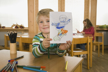 Deutschland, Kinder im Kinderzimmer, Junge (4-5) im Vordergrund hält Bild, lächelnd, Porträt - RNF00157