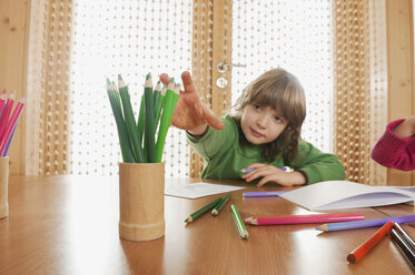 Deutschland, Junge (6-7) im Kinderzimmer am Tisch sitzend, nach Buntstift greifend, Porträt - RNF00154