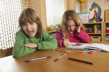 Deutschland, Junge (6-7) und Mädchen (4-5) im Kinderzimmer Junge streckt Zunge heraus, Porträt - RNF00150