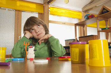 Deutschland, Junge (6-7) am Tisch im Kinderzimmer sitzend, nach oben schauend, Porträt - RNF00145