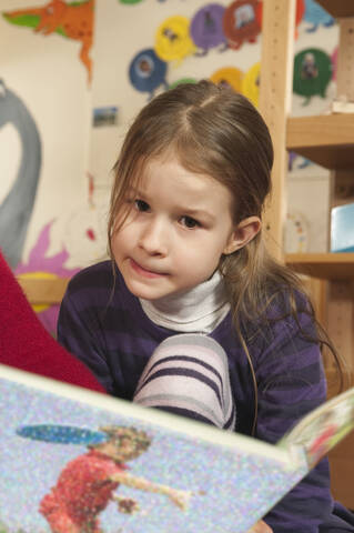 Deutschland, Mädchen (4-5) im Kinderzimmer beim Lesen eines Buches, Porträt, lizenzfreies Stockfoto