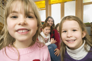 Deutschland, Zwei Mädchen (3-5) im Vordergrund schauen in die Kamera, Erzieherin mit Kindern im Hintergrund - RNF00123