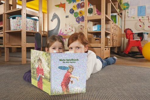 Deutschland, Zwei Mädchen (4-5), (6-7) im Kinderzimmer auf Teppich liegend und ein Buch lesend, Portrait - RNF00104