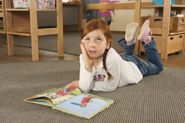 Deutschland, Mädchen (6-7) im Kinderzimmer auf dem Teppich liegend und ein Buch lesend - RNF00103