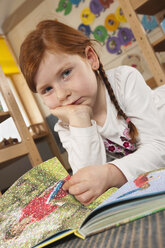 Deutschland, Mädchen (6-7) im Kinderzimmer beim Lesen eines Buches, Hand am Kinn, Porträt, Nahaufnahme - RNF00102