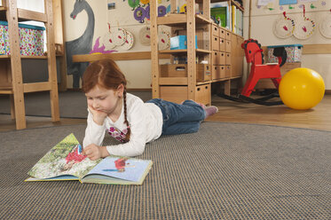 Deutschland, Mädchen (6-7) im Kinderzimmer auf dem Teppich liegend und ein Buch lesend - RNF00101