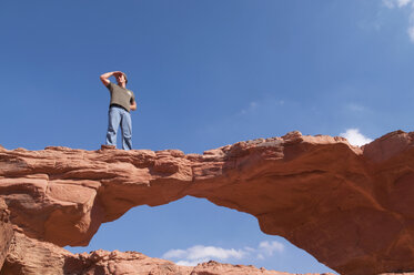 Man standing on rock formation, shielding eyes - NHF01194