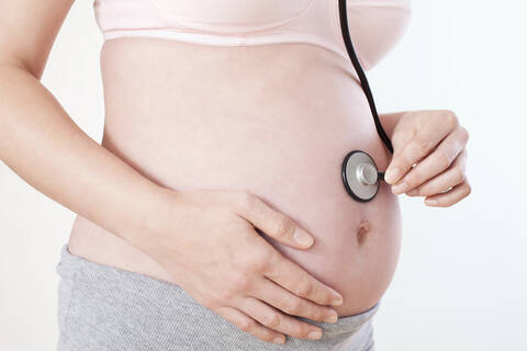 Pregnant woman holding stethoscope on belly, mid section, close-up stock photo