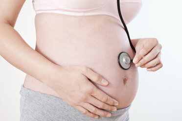 Pregnant woman holding stethoscope on belly, mid section, close-up - MAEF02051