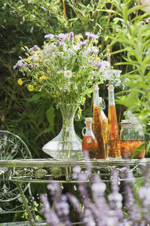 Österreich, Salzburger Land, Blumenvase und Kräuteressenzen in Flaschen auf Tisch im Garten - HHF03163