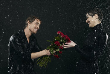 Männer bieten Frauen bei Regen einen Blumenstrauß an. - FMKF00047