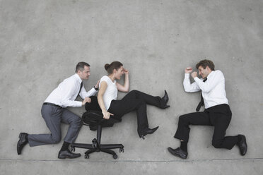Three business people, business man pushing businesswoman in office chair, side view, elevated view - BAEF00079