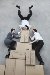 Drei Geschäftsleute auf Pappkartons, Mann macht Handstand, lächelnd, Porträt, Blick von oben - BAEF00034