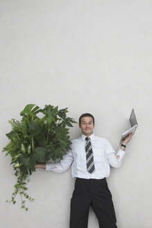 Businessman holding laptop and Foliage Plants, smiling, portrait - BAEF00013