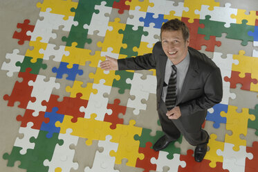 Geschäftsmann stehend auf Puzzle, lächelnd, Porträt, Blick von oben - ASF03970