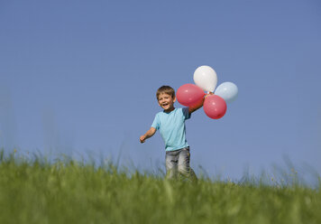 Österreich, Mondsee, Junge (2-3) läuft mit Luftballons durch eine Wiese - WWF01261