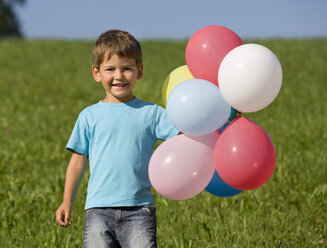 Junge (2-3) steht auf einer Wiese und hält Luftballons, lächelnd, Porträt - WWF01259