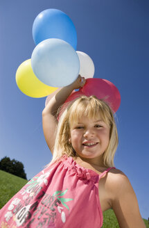 Österreich, Mondsee, Mädchen (4-5) stehend auf Wiese mit Luftballons, lächelnd, Porträt - WWF01255