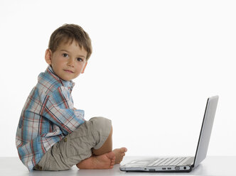 Junge (2-3) sitzend mit Laptop vor weißem Hintergrund, Porträt, Nahaufnahme - WWF01218