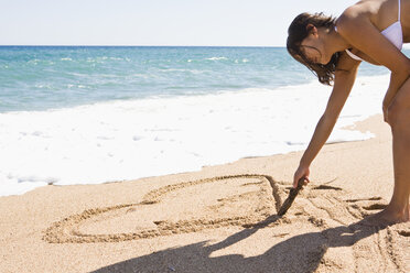 France, Corsica, Woman drawing heart shape in sand on beach - SSF00054