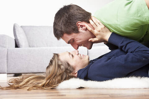 Young couple lying on floor, rubbing noses, side view stock photo