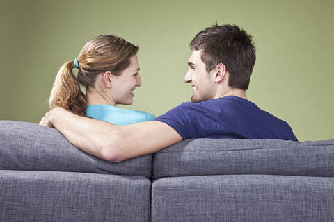 Junges Paar sitzt auf der Couch und lächelt sich gegenseitig an, Rückansicht, lizenzfreies Stockfoto