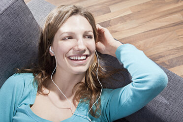 Frau entspannt sich auf der Couch und hört Musik, lächelnd - SSF00014