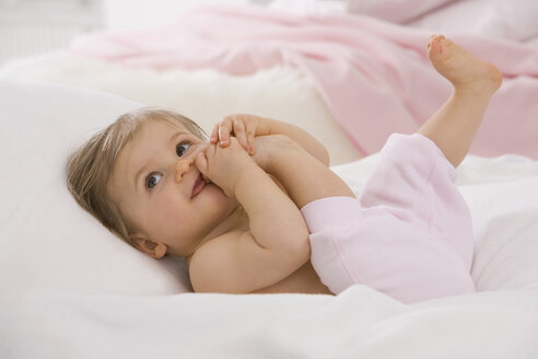 Baby-Mädchen (6-11 Monate) nimmt sein Bein in den Mund und schaut weg - SMOF00441