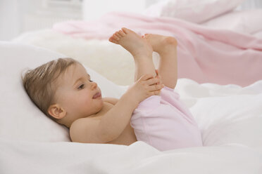 Baby-Mädchen (6-11 Monate) streckt die Zunge heraus und hält die Füße hoch - SMOF00440