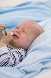 Baby boy (6-11 months) holding baby bottle, crying - SMOF00412