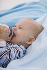 Baby boy (6-11 months) holding baby bottle, looking up - SMOF00407