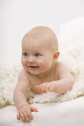 Baby boy (6-11 months) lying on bed, smiling, looking away - SMOF00393