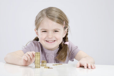 Girl (4-5) counting stack of coins, smiling, portrait - RBF00232