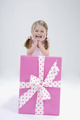 Mädchen (4-5) lehnt sich lächelnd an einen Geschenkkarton, Porträt - RBF00224