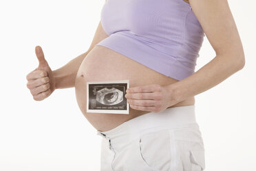 Pregnant woman holding sonogram image, showing thumbs up sign, mid section - RBF00213