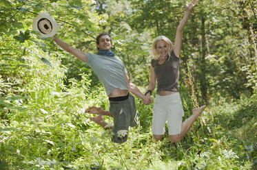 Junges Paar hält sich an den Händen und springt im Wald - HHF03255