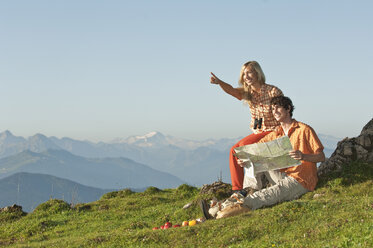 Junges Paar sitzt auf einem Berggipfel, der Mann hält eine Karte in der Hand und lächelt. - HHF03232