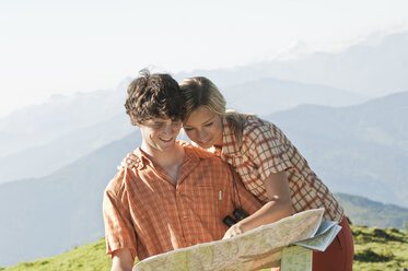 Junges Paar, das auf einem Berggipfel lächelnd eine Karte betrachtet. - HHF03229