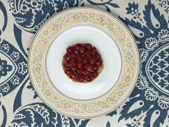 Raspberry tartlet in plate against patterned background - AKF00147