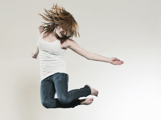 Teenage girl (16-17) jumping against gray background - FMKF00143