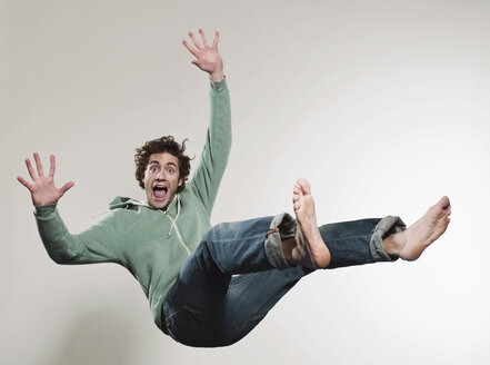 Man falling against grey background, mouth open, portrait - FMKF00129