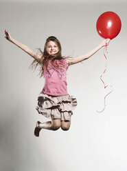 Girl (8-9) jumping with holding balloon, smiling, portrait - FMKF00125