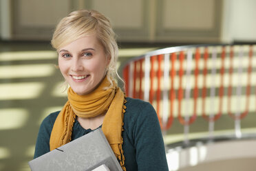 Deutschland, Leipzig, Junge Frau mit Büchern im Hausflur stehend, lächelnd, Porträt - BABF00602