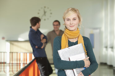 Deutschland, Leipzig, Junge Frau mit Buch in der Hand, im Hintergrund stehen Studenten - BABF00601