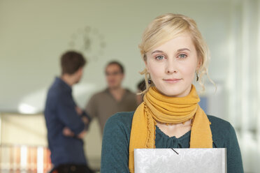 Deutschland, Leipzig, Junge Frau mit Buch in der Hand, im Hintergrund stehen Studenten - BABF00600