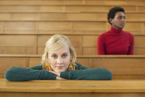 Deutschland, Leipzig, Student lehnt sich an Schreibtisch, Frau sitzt im Hintergrund, lizenzfreies Stockfoto