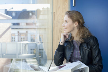 Germany, Leipzig, Young woman looking through window, smiling - BABF00529