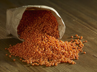 Red lentils spilling on wooden surface - SRSF00163