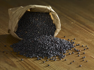 Black lentils spilled on wooden surface - SRSF00159